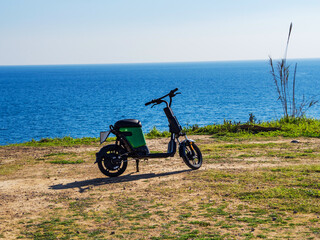 A black rental moped stands on the shore against the backdrop of the blue sea. Sunny weather.