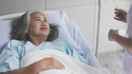 Asian nurse checks IV bag for elderly female patient in hospital room