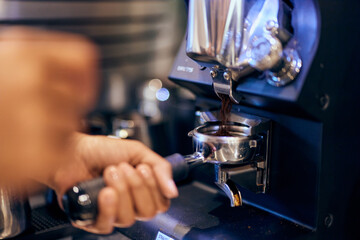A barista holding a handle with a ground coffee pouring into a portafilter with a grinder.