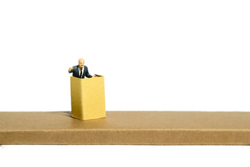 Miniature tiny people toy figure photography. A men with suit given speech standing at stage on...