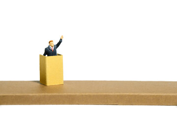 Miniature tiny people toy figure photography. A men with suit given speech standing at stage on...