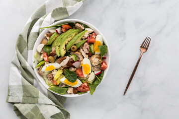 A healthy tossed salad topped with shredded chicken and sliced egg and avocado.