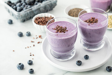 Healthy blueberry protein smoothies surrounded by ingredients used to make it.
