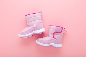 New warm waterproof winter boots on light pink table background. Pastel color. Children footwear....