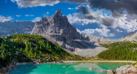 Fototapeta na wymiar Panoramic View of Turquoise Lake in Dolomites, Italy with Solitary Figure and Snow-Capped Peaks