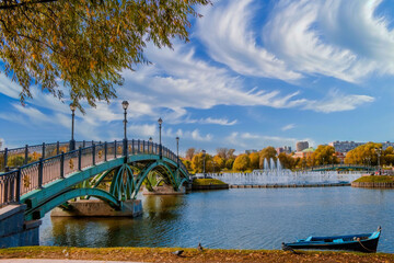 Serene Urban Park Scene with Blue Rowboat, Teal Bridge, Water Fountains, and Autumn Trees