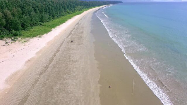 Drone view of a large, wide and quiet tropical sandy beach surrounded by green foliage