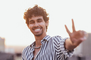 An attractive curly-haired guy in a striped shirt smiles against the backdrop