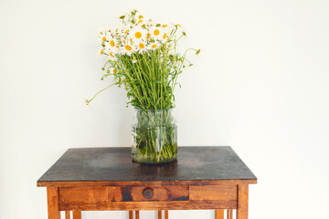 A large bouquet of chamomiles stands in a glass vase on an old vintage wooden table.