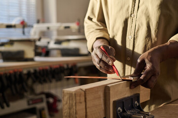 Close up of senior carpenter carefully measuring wood and putting pencil marks in sunlit workshop