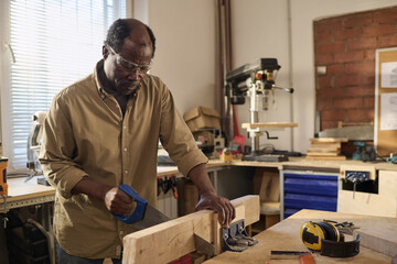 Portrait of African American senior man cutting wood while building furniture in sunlit workshop