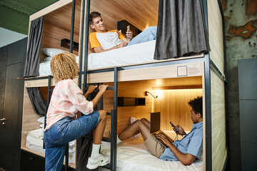 african american woman near multiethnic buddies with digital devices on double-decker bed in hostel - obrazy, fototapety, plakaty