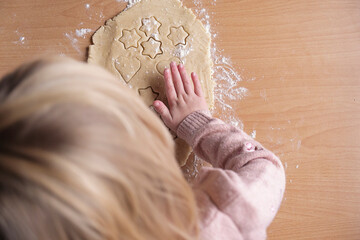 Girl's hands hold a cookie cutter and apply it to the dough. View from above. Home cooking of biscuits. Leisure concept for children. Cookie making process