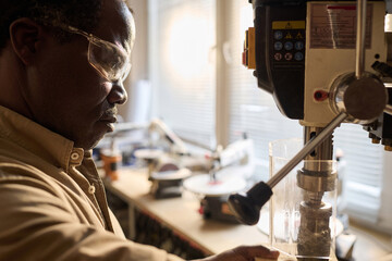 Side view closeup of Black man in protective glasses using machine tools in carpenters workshop