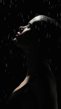 Vertical silhouette elegant female standing under rain at night. Seductive woman, gymnast dancer wearing swimsuit, raindrops splashes, water drops roll down sexy body in shower, black background	
