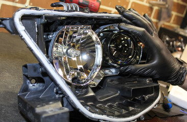 Fototapeta premium The car mechanic installs the lens in the headlight housing. The concept of a car service. Installation of BI-LED lenses in the headlight. BI-LED lens. Restoration of optics.