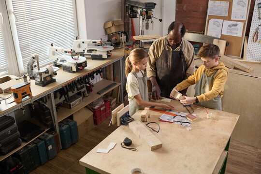 High angle view at carpenter teaching young kids in crafting workshop for children, copy space