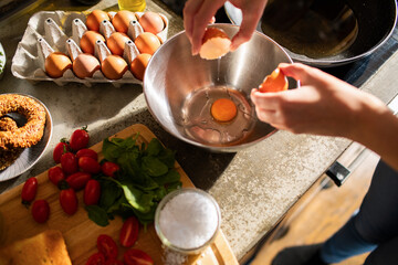 Woman cracking an egg into a bowl for cooking at home kitchen