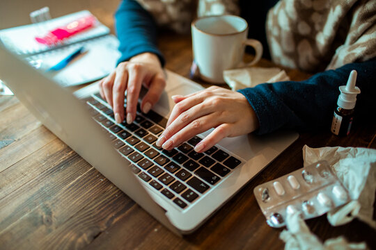 Close-up of hands typing on laptop with cold medicine on table