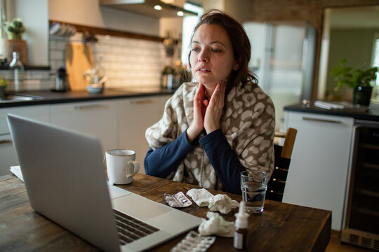 Woman feeling sick with sore throat and flu symptoms working on laptop at home