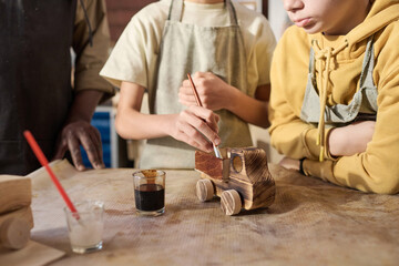 Close up of two children painting wooden toys model in carpenting workshop for kids, copy space