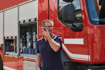 A dedicated firefighter, captured in a moment of communication, stands before a modern firetruck,...