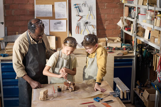 High angle view at children painting wooden toy model in carpenting workshop, Black teacher watching