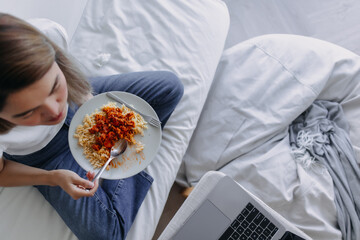 Top view of Asian woman eating pasta while watching movie or series from notebook, sitting on white...