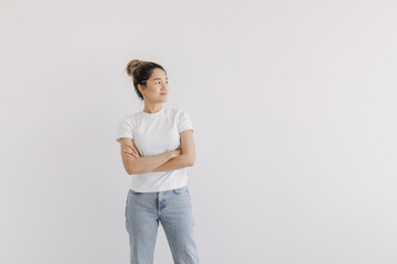 Asian women wear white and jeans, standing and smiling, crossing arms while looking at empty space, isolated over white background wall.