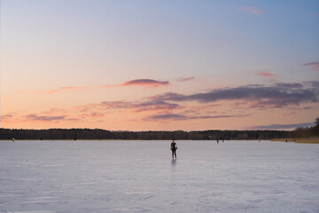 A girl skates on ice on frozen Lake Harku on a winter evening. Nature of Estonia.