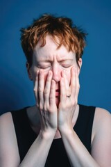hands on face, woman with mental health issues and depression in studio isolated on a blue background