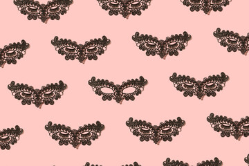 Black lace eye mask for a costume party. Creative pattern on pastel pink peach background.