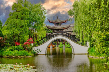 Traditional Chinese Garden with High-Arched White Bridge, Lush Greenery, and Serene Pond...