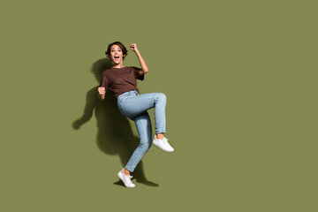 Full length photo of ecstatic satisfied girl wear oversize t-shirt denim pants scream yes win gambling isolated on green color background
