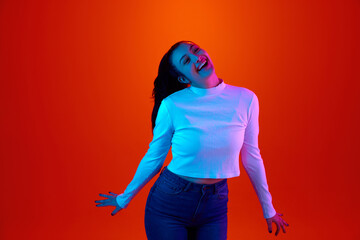 Laughing. Portrait of young attractive girl, student looking at camera against gradient orange color background in neon light. Concept of beauty, art, fashion, youth, sales and ad, education