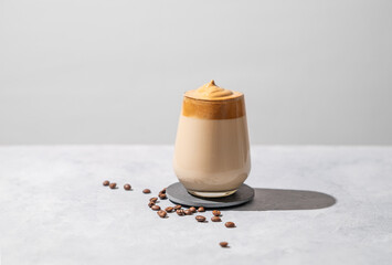Dalgona coffee. Whipped instant coffee in a glass with beans and shadow on a light background.