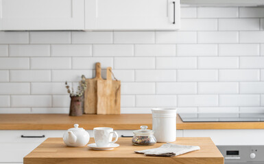 Fototapeta na wymiar Wooden oak table with a cup of tea and a kettle in front of the kitchen with a white brick background.