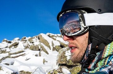 Skier's snowboarder equipment: helmet mask, glasses. Reflection in ski goggles, snowy stones. Man...