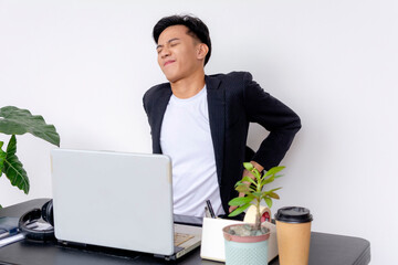 A college student or young employee at his desk straining from lower back pain. Of southeast asian...