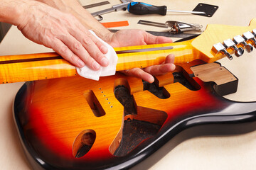 Guitar master polishes neck of electric guitar.