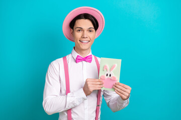 Photo of handsome nice guy wear white shirt pink headwear bow tie hands hold postcard with bunny isolated on blue color background