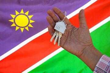 Hand shows the keys to the apartment on background of flag Namibia. Keys to the apartment in a...