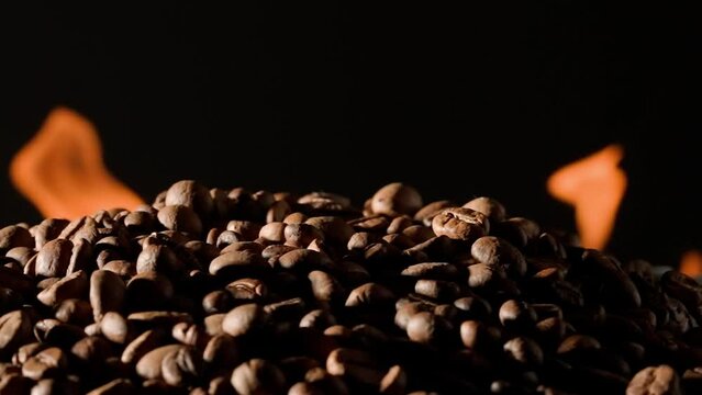 Coffee beans rotate on a black studio background with burning tongues of flame. The process of roasting coffee to make an invigorating drink. Advertising concept for a coffee shop or restaurant.