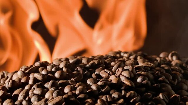 Coffee beans rotate on a black studio background with burning tongues of flame. The process of roasting coffee to make an invigorating drink. Advertising concept for a coffee shop or restaurant.