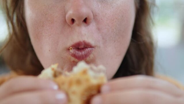 Closeup of chewing mouth of plus size woman with freckles on her cheeks. Female caucasian person bites and eats flatbread. Harmful high calorie fatty foods that contribute to obesity.