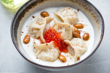 Middle closeup of vareniki or boiled dumplings served with white yogurt and red caviar in a grey bowl, horizontal shot, selective focus