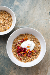 Granola bowls with yogurt, pomegranate seeds and nuts, above view on a beige granite background, vertical shot with space