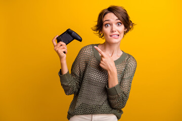 Naklejka premium Photo of lovely young lady point amazed joystick play station dressed stylish knitted khaki garment isolated on yellow color background