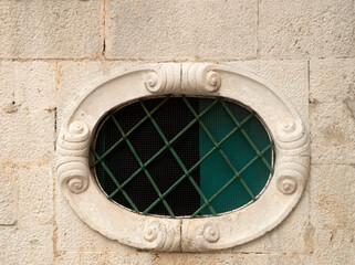 Old elliptical window with metal grill on stone facade in Montenegro