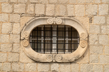 Old elliptical window with metal grill on stone facade in Montenegro